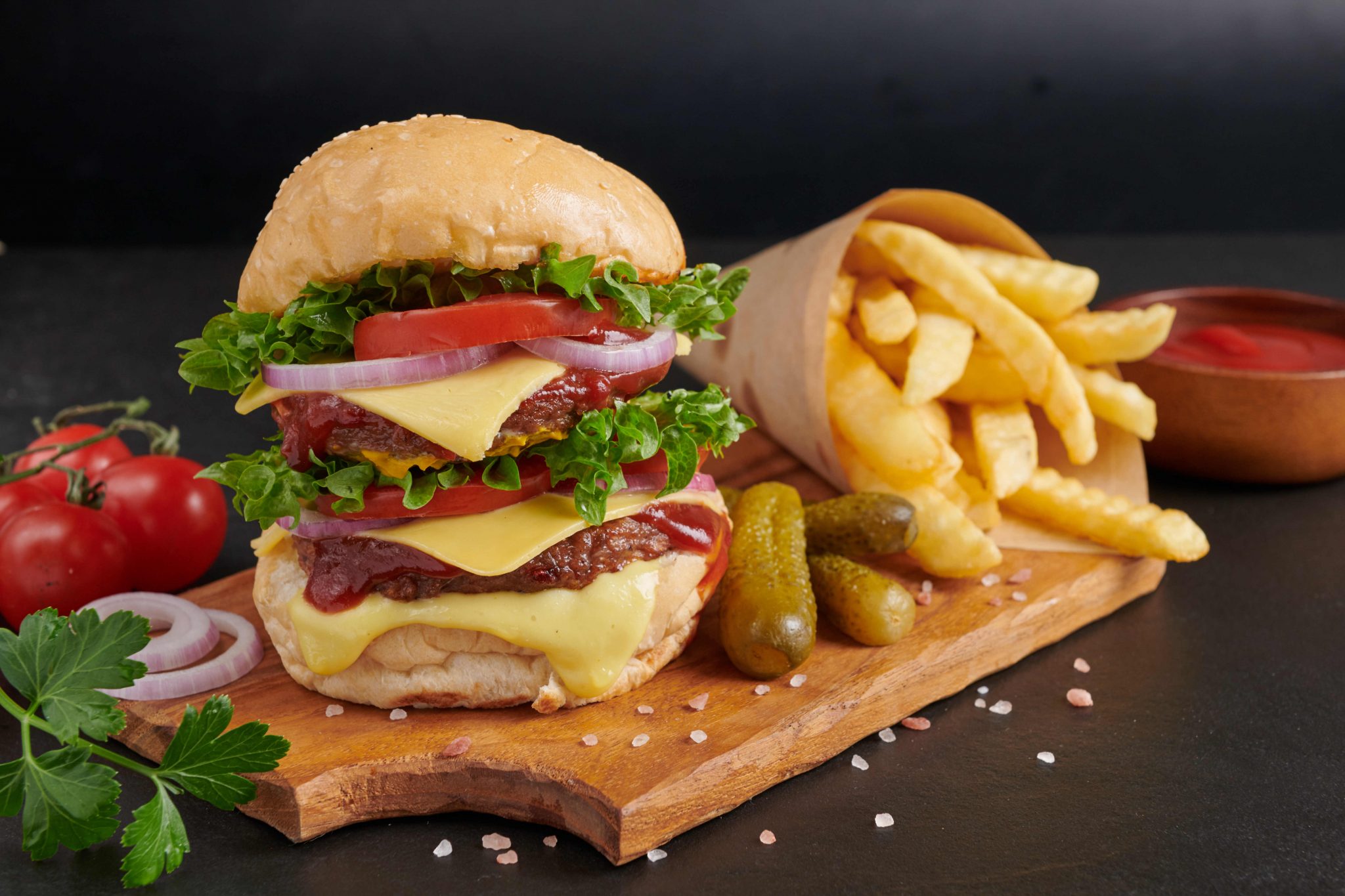 Homemade hamburger or burger with fresh vegetables and cheese lettuce and mayonnaise served, French fries on pieces of brown paper on black stone table . concept of fast food and junk food